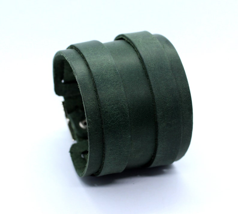 May include: A dark green leather cuff bracelet with multiple layers of leather. The bracelet has a silver buckle and stitching.