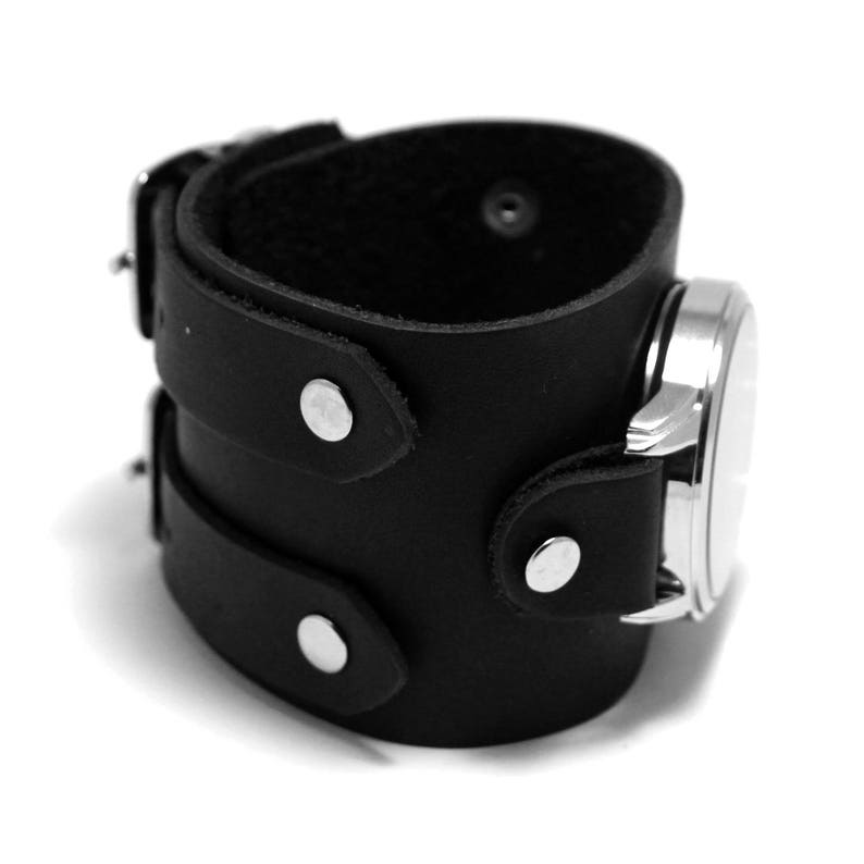 May include: Black leather cuff watch band with silver accents and a buckle closure.