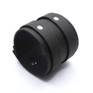 May include: A black leather cuff bracelet with silver metal accents. The bracelet is made of three layers of leather and has a simple, minimalist design.