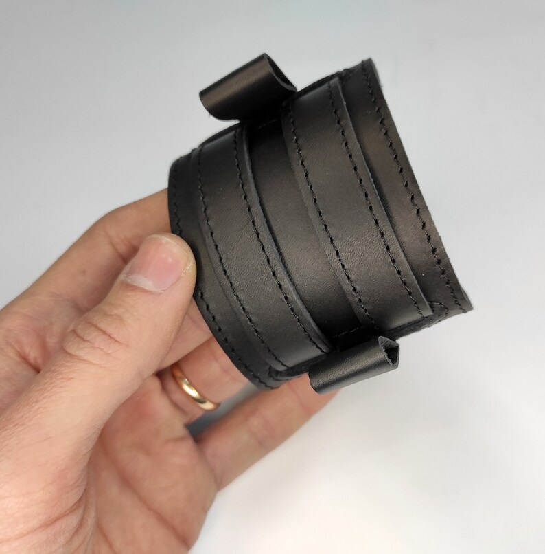 May include: Black leather wristband with multiple stitched layers and a fold-over closure.
