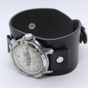 Peut inclure: Une montre-bracelet argentée avec un bracelet en cuir noir. Le cadran de la montre a un fond blanc avec des chiffres noirs et une étoile rouge. Le cadran de la montre présente également une image en noir et blanc d'un char.