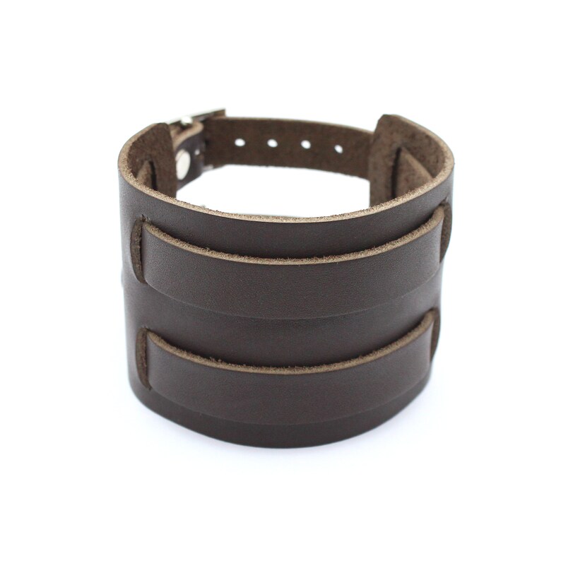 May include: A brown leather cuff bracelet with a buckle fastening. The bracelet has three layers of leather.
