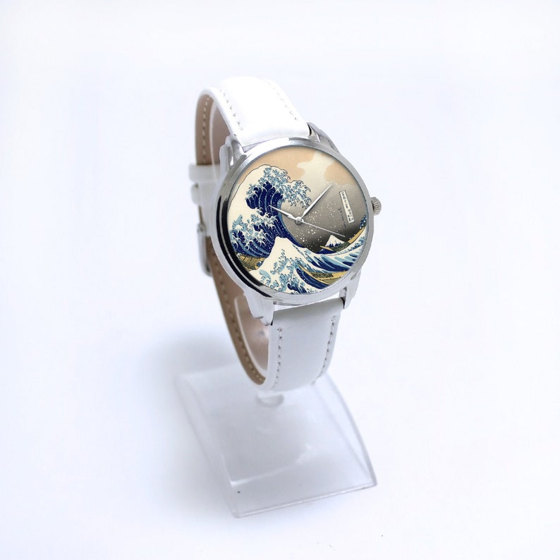 May include: A white wristwatch with a silver band and a round face featuring a print of "The Great Wave off Kanagawa" by Katsushika Hokusai.