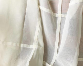 May include: A sheer off-white garment featuring a lightweight, translucent fabric construction. The piece is detailed with visible vertical and horizontal seams that create a structured grid pattern across the surface of the material.
