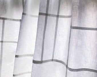 May include: White linen curtains featuring a subtle grid pattern of horizontal and vertical lines. The fabric is semi-sheer, allowing light to pass through. The curtains are suspended from a white rod using white circular rings and clips.