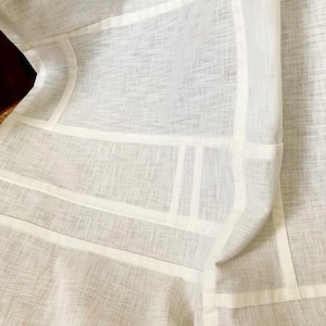 May include: A white fabric garment featuring a visible woven texture and a geometric pattern created by thick, opaque white fabric strips sewn onto a semi-sheer white base material. The design consists of intersecting horizontal and vertical lines.