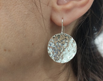 Puede incluir: Pendientes de círculo martillados de plata. Los pendientes son de diseño simple y moderno con un acabado texturizado.