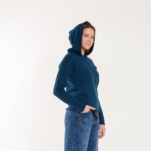 Op de afbeelding: Een tealblauwe hoodie met lange mouwen en een ontspannen pasvorm. Het model draagt ​​een blauwe jeans en staat op een witte achtergrond.