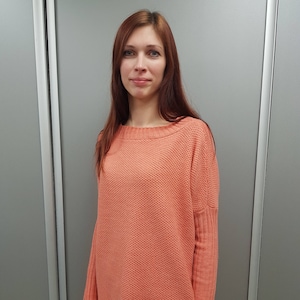 May include: A coral colored knitted sweater with a loose fit and long sleeves.