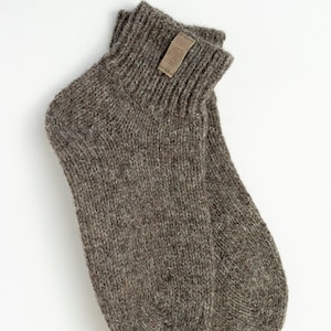 Könnte beinhalten: Ein Paar braune Wollsocken mit einem kleinen braunen Lederanhänger mit der Aufschrift "Woolmark" auf der Oberseite einer Socke.