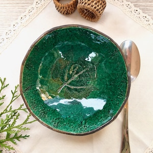 May include: A green ceramic bowl with a leaf design. The bowl is on a white tablecloth with lace trim.