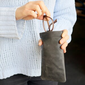 May include: A person is holding a black leather glasses case with a pair of glasses inside. The case has a flap that closes with a snap.