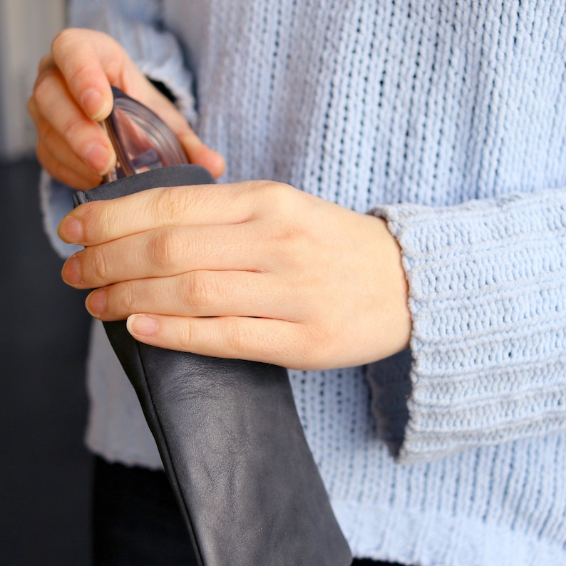 May include: A person's hand holding a black leather glasses case with a pair of glasses inside.