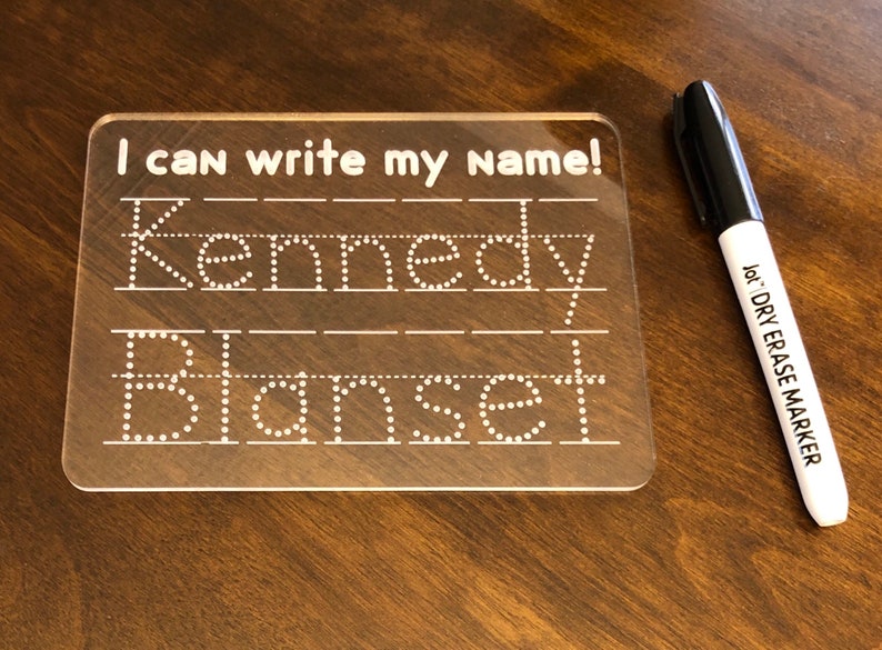Puede incluir: Una pizarra de borrado en seco de pl&aacute;stico transparente con el texto "I can write my name!" y los nombres "Kennedy" y "Blansett" escritos en l&iacute;neas punteadas. Se incluye un marcador de borrado en seco negro.