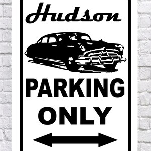 May include: A rectangular white metal sign with a black border. The sign features the word "Hudson" in cursive above a black silhouette of a classic car. Below the car, the words "PARKING ONLY" are displayed in bold, with arrows pointing left and right.