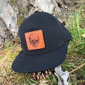 May include: Black baseball cap with a brown leather patch featuring a skull design.