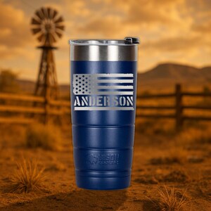 K&ouml;nnte beinhalten: Ein blauer und silberner Edelstahlbecher mit einem abgenutzten amerikanischen Flaggenmuster und dem Namen "Anderson" auf der Vorderseite eingraviert.