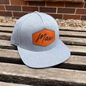 May include: A gray and brown baseball cap with a leather patch that says "Max" on it.