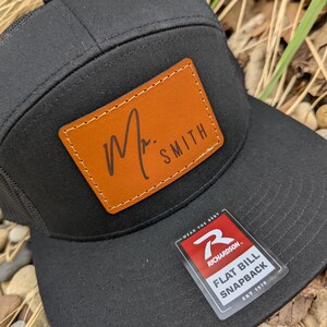 May include: Black and brown flat bill snapback hat with a leather patch that says "M. SMITH" and a Richardson logo on the side.