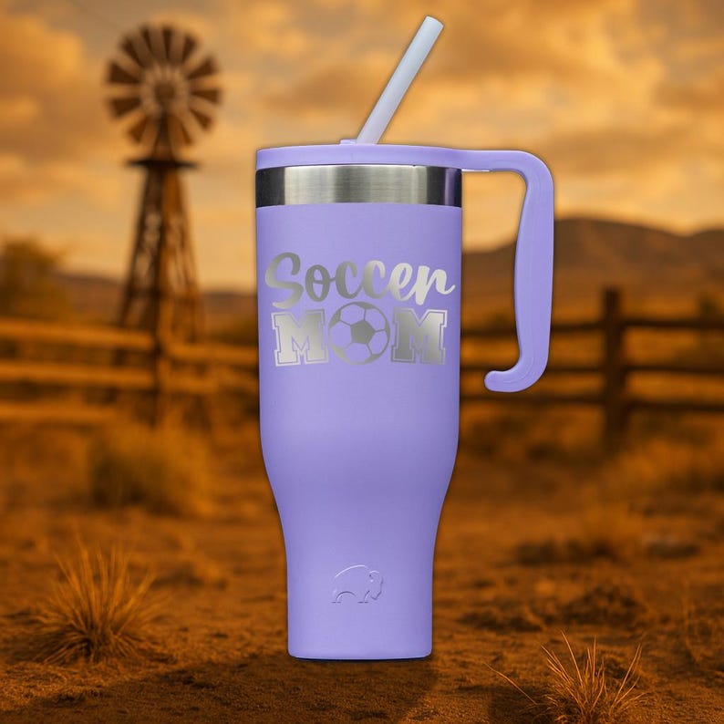 May include: A purple stainless steel travel mug with a handle and a straw. The mug has a silver design that says "Soccer Mom" with a soccer ball.
