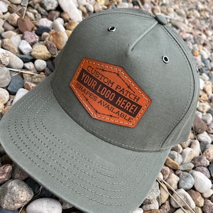 May include: A green baseball cap with a brown leather patch that says "CUSTOM PATCH YOUR LOGO HERE! SHAPES AVAILABLE".