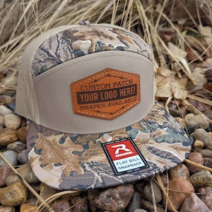 May include: A tan and brown camouflage flat bill snapback hat with a brown leather patch that says "CUSTOM PATCH YOUR LOGO HERE! SHAPES AVAILABLE". The hat also has a red and black logo that says "R RICHARDSON FLAT BILL SNAPBACK EST 1918".