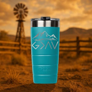 Op de afbeelding: Een turquoise roestvrijstalen tumbler met een zilveren deksel. De tumbler heeft een bergketenontwerp en de woorden "God is groter dan" in zilveren letters.