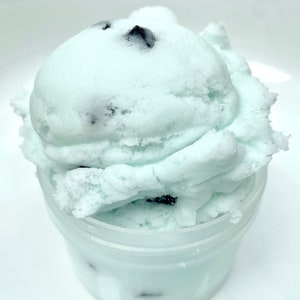 May include: A close-up of a light blue and white slime with dark brown chocolate chips in a clear plastic container.
