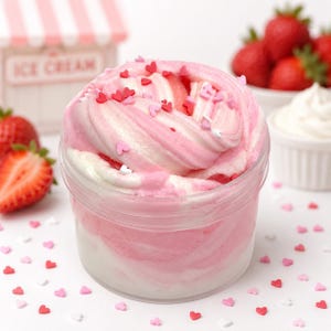 May include: A clear plastic jar filled with swirled pink and white slime, topped with small red and pink heart-shaped sprinkles. The texture appears thick and creamy, with distinct layers of colour blended together throughout the container.
