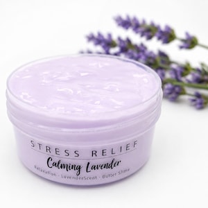 May include: A round, clear plastic container filled with light purple butter slime. The label reads STRESS RELIEF Calming Lavender, Relaxation, LavenderScent, Butter Slime. A sprig of purple lavender flowers is positioned behind the container.