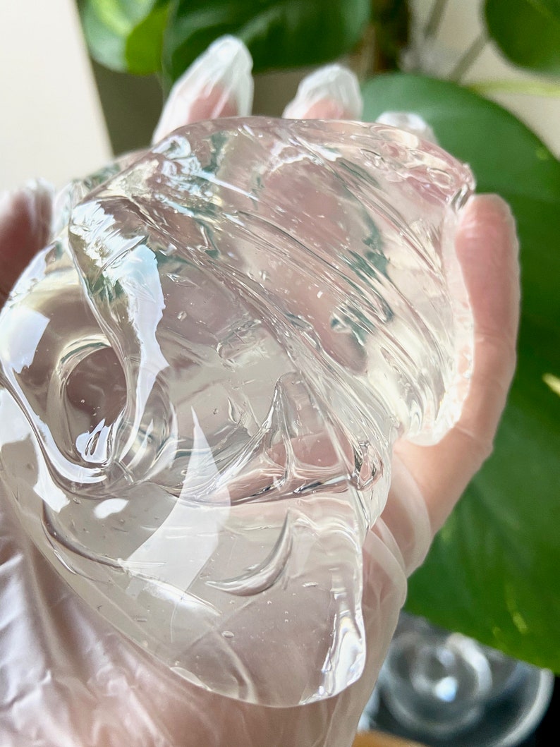 May include: A clear, translucent gel substance with a smooth, viscous texture. The gel is being held in a gloved hand.