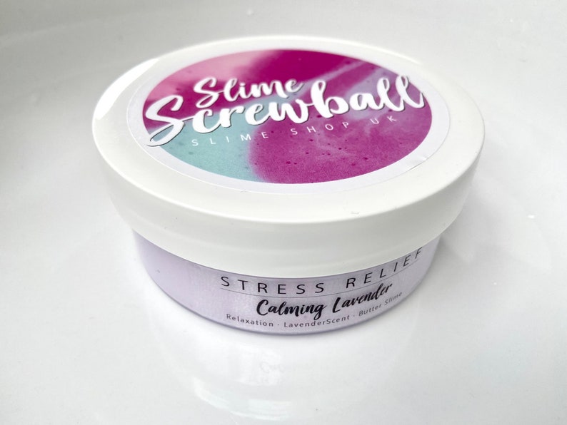 May include: A white container of lavender-scented slime. The lid features a colorful design with the text "Slime Screwball SLIME SHOP UK." The label reads "Stress Relief Calming Lavender" with additional text about relaxation and butter slime.