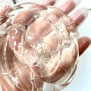 May include: A clear, translucent, gel-like substance in a gloved hand. The gel is thick and viscous, with a slightly cloudy appearance.