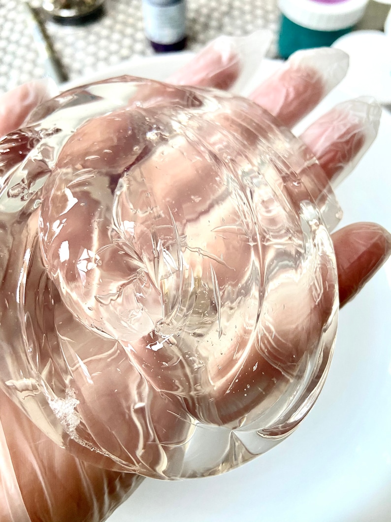 May include: A clear, translucent, gel-like substance in a gloved hand. The gel is thick and viscous, with a slightly cloudy appearance.