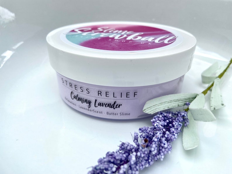 May include: A white jar of lavender-scented butter slime with the text "Stress Relief Calming Lavender". The jar is decorated with a sprig of lavender. The jar has a white lid with the text "Slime Screwball Shop UK".