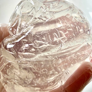 May include: A clear, viscous gel substance in a gloved hand. The gel is thick and has a smooth, shiny surface.
