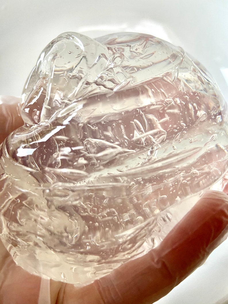 May include: A clear, viscous gel substance in a gloved hand. The gel is thick and has a smooth, shiny surface.