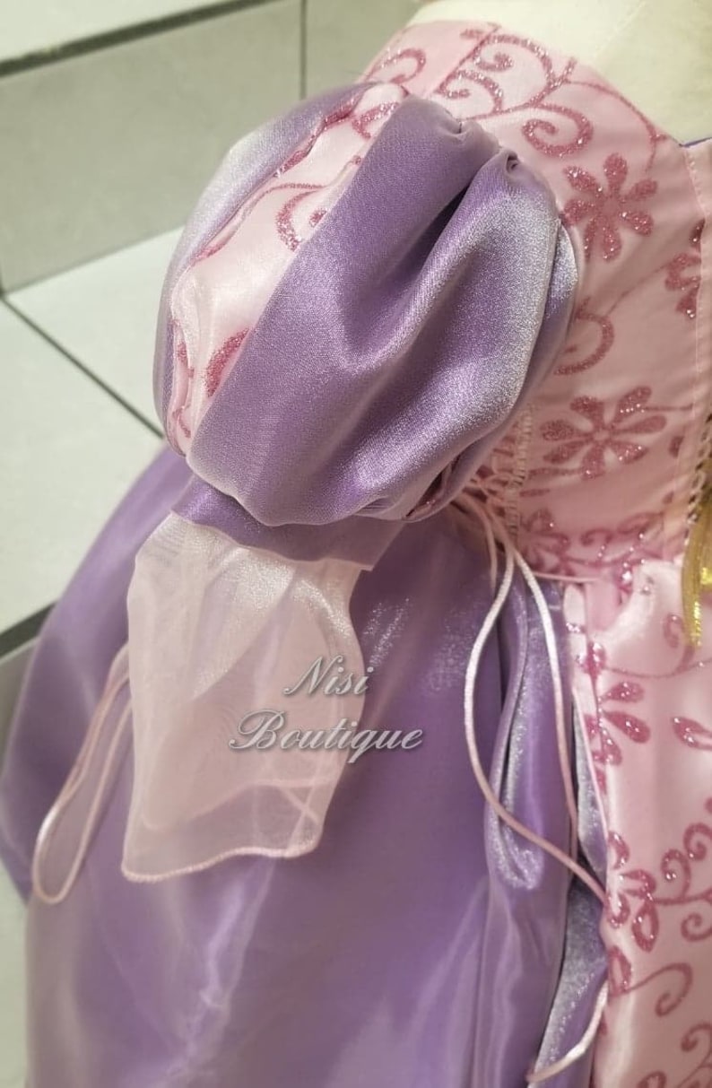 May include: A purple and pink satin dress with a puffed sleeve and a lace trim. The dress has a lace-up back and a pink satin sash.