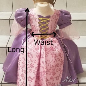 May include: A purple and pink princess dress with a gold bodice and a floral pattern. The dress has a long skirt and a waist measurement. The dress is labeled "Nisi Boutique".