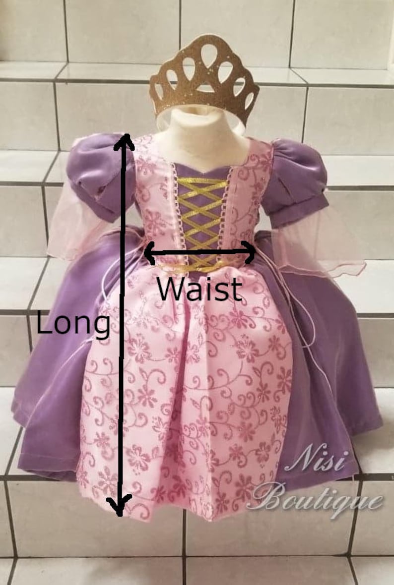 May include: A purple and pink princess dress with a gold bodice and a floral pattern. The dress has a long skirt and a waist measurement. The dress is labeled "Nisi Boutique".