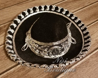 May include: A black sombrero with silver trim and embroidery. The hat has a wide brim and a tall crown. The embroidery features a floral design.