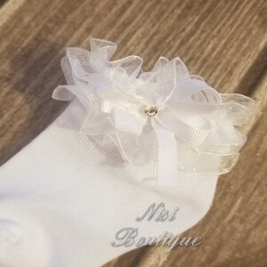 May include: White socks with a white lace ruffle and a small rhinestone embellishment. The socks have the text "Nisi Boutique" on the side.