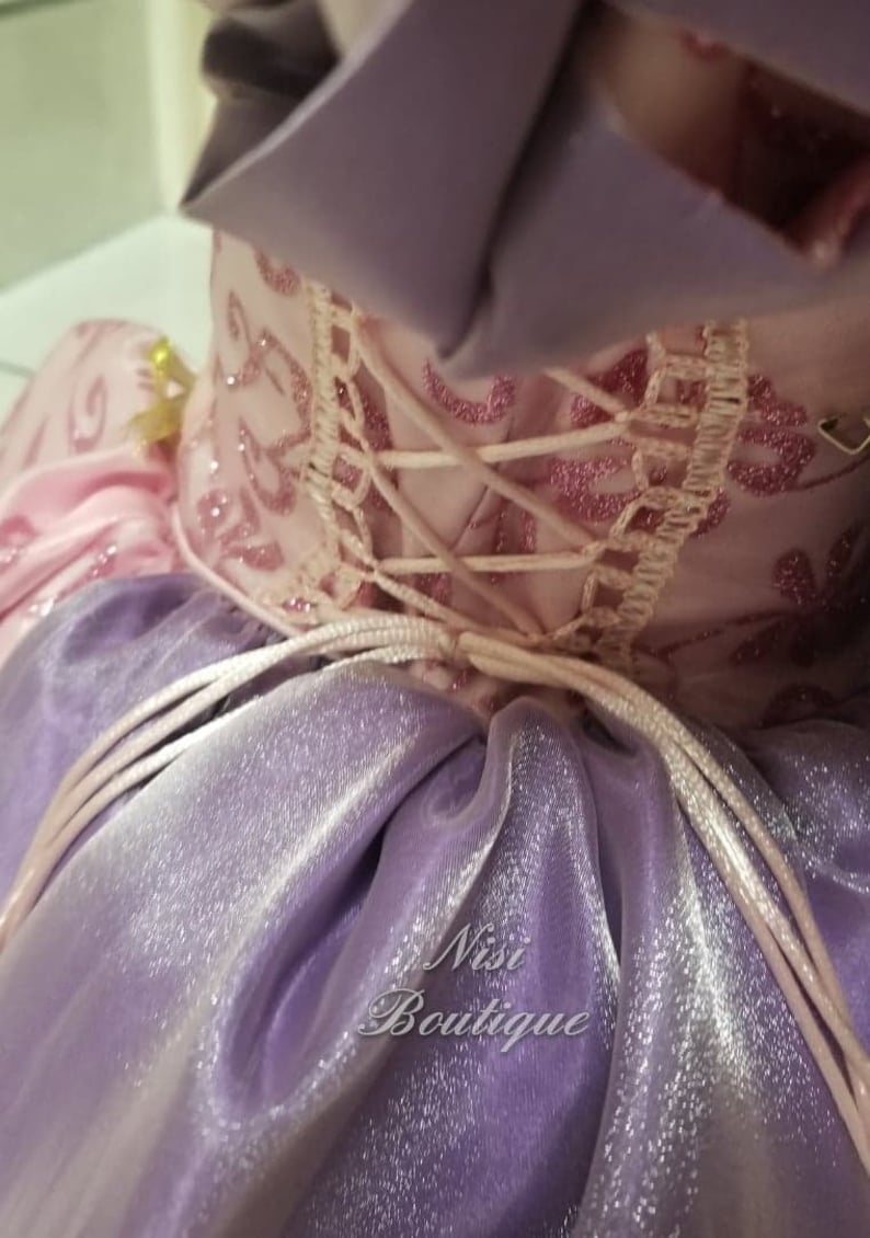 May include: A purple and pink dress with a lace-up back and a tulle skirt. The dress has a sparkly finish and the text "Nisi Boutique" is visible on the skirt.