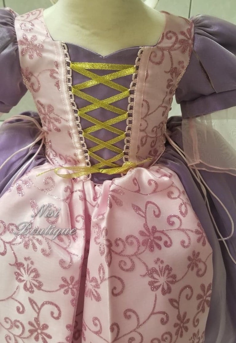 May include: A purple and pink princess dress with a gold ribbon corset and a floral pattern. The dress has a tulle overlay and is perfect for a little girl's costume.