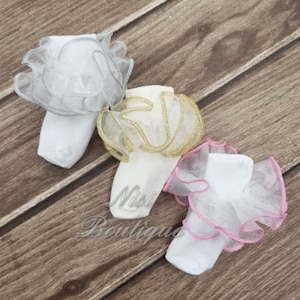 May include: Three pairs of white baby socks with ruffled tulle trim. The tulle is silver, gold, and pink.
