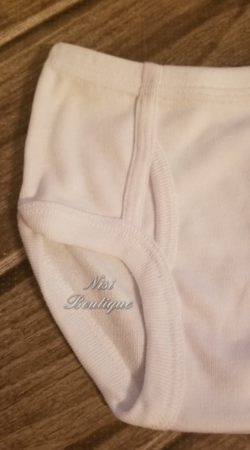 Pode incluir: Roupa interior de algod&atilde;o branco com uma costura dupla. A roupa interior tem o texto "Nisi Boutique" impresso na frente.