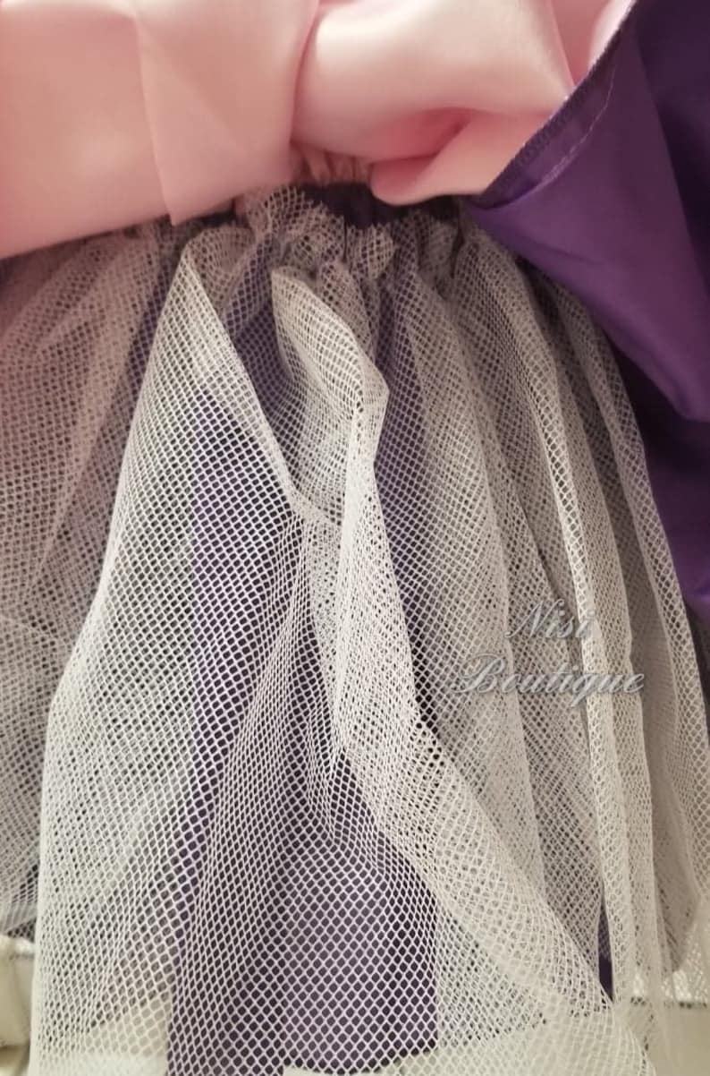 May include: Close-up of a white tulle fabric layered over a purple satin fabric. The tulle is a fine mesh with a delicate texture.