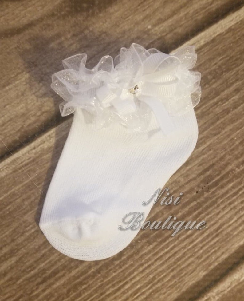 May include: White baby socks with a white lace ruffle and a small rhinestone bow.