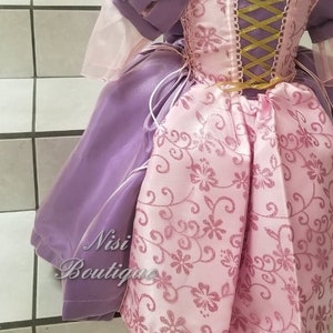 May include: A purple and pink princess dress with a gold ribbon and lace up back. The dress has a floral pattern and is made of satin.