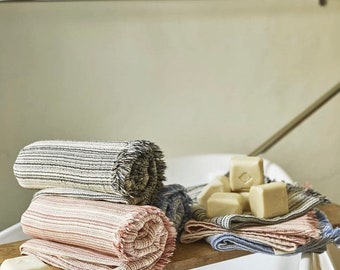Op de afbeelding: Drie gerolde handdoeken in verschillende kleuren en patronen, met een stapel zeepjes op een houten oppervlak.